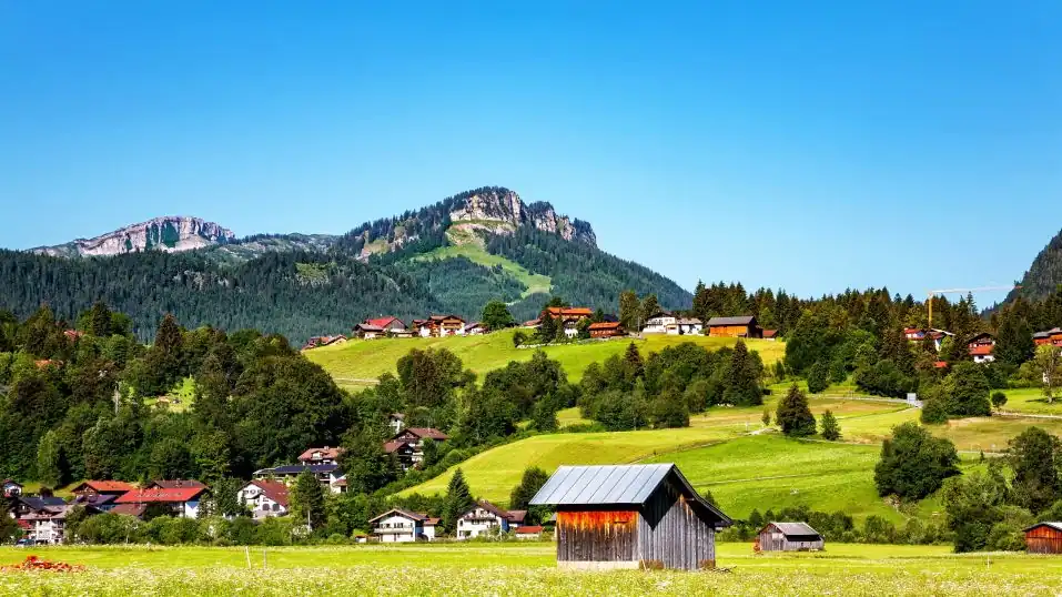 Landschaft im Allgäu: im Vordergrund Häuser und Wiesen, dahinter hohe Berge am Horizont