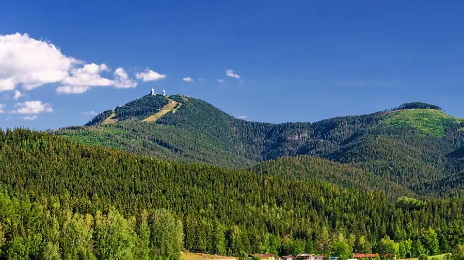 Panorama im Bayerischen Wald: blauer Himmel über hügeligen Wäldern, im Hintergrund der Große Arber