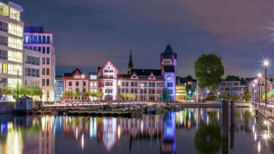 Hörder Burg in Dortmund, beleuchtet bei Nacht, davor der Phoenix-See mit Booten am Kai