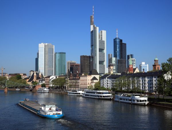 die Skyline von Frankfurt unter blauem Himmel, im Vordergrund der Main mit Schiffen