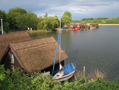 Foto schilfgedeckte Häuser am Ufer der Müritz, ein Segelboot vor Anker