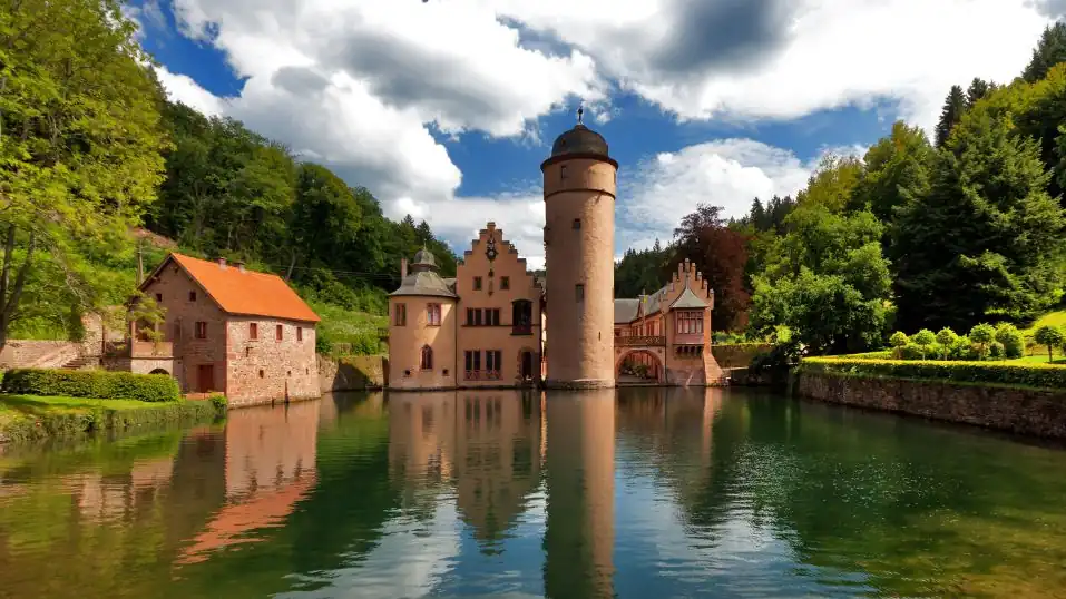 Schloss Mespelbrunn im Spessart, umringt von Wäldern, im Vordergrund der Schlossteich